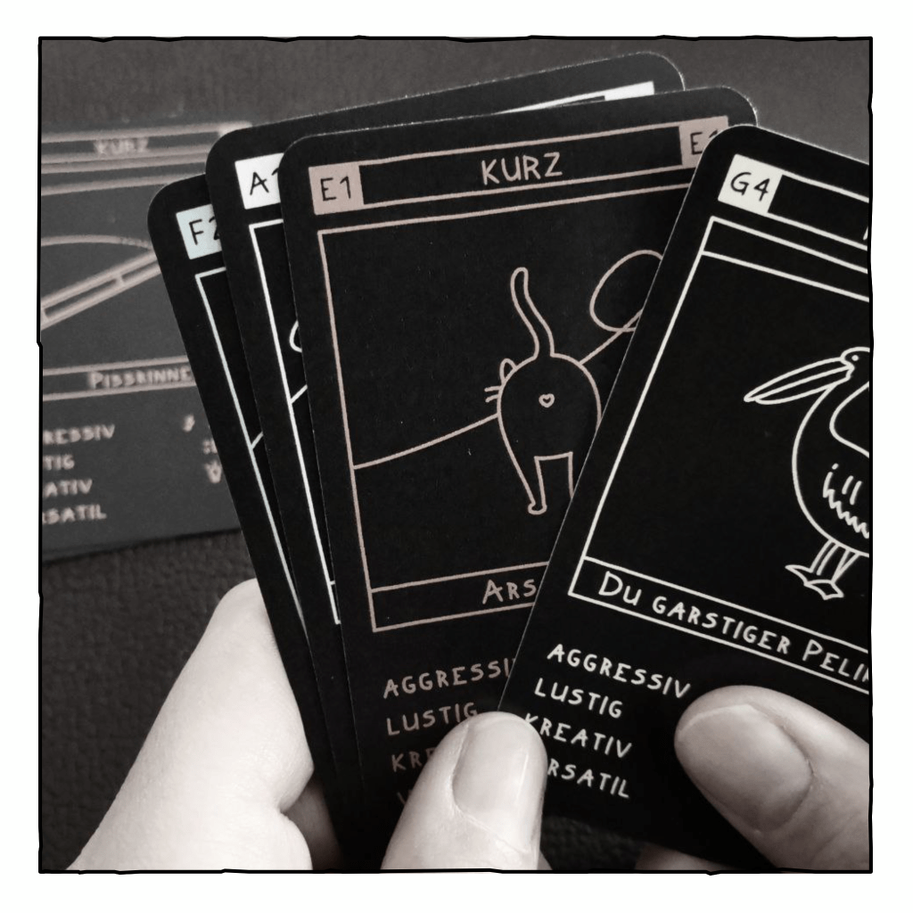 Eine Person hält vier Karten in der Hand. Die oberste Karte zeigt die Beleidigung "garstiger Pelikan".